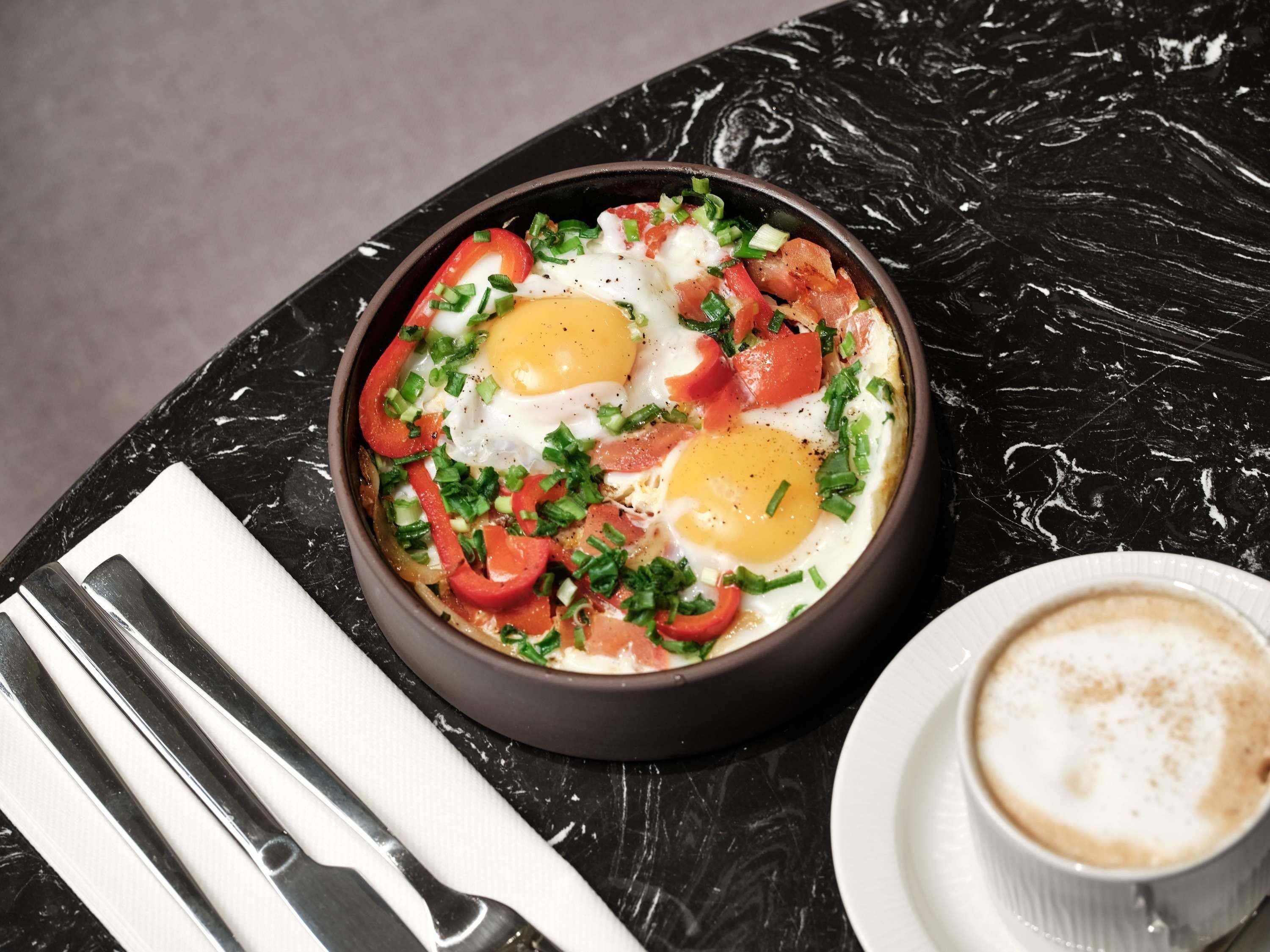 A breakfast dish with eggs, tomatoes, and green onions on a black plate.