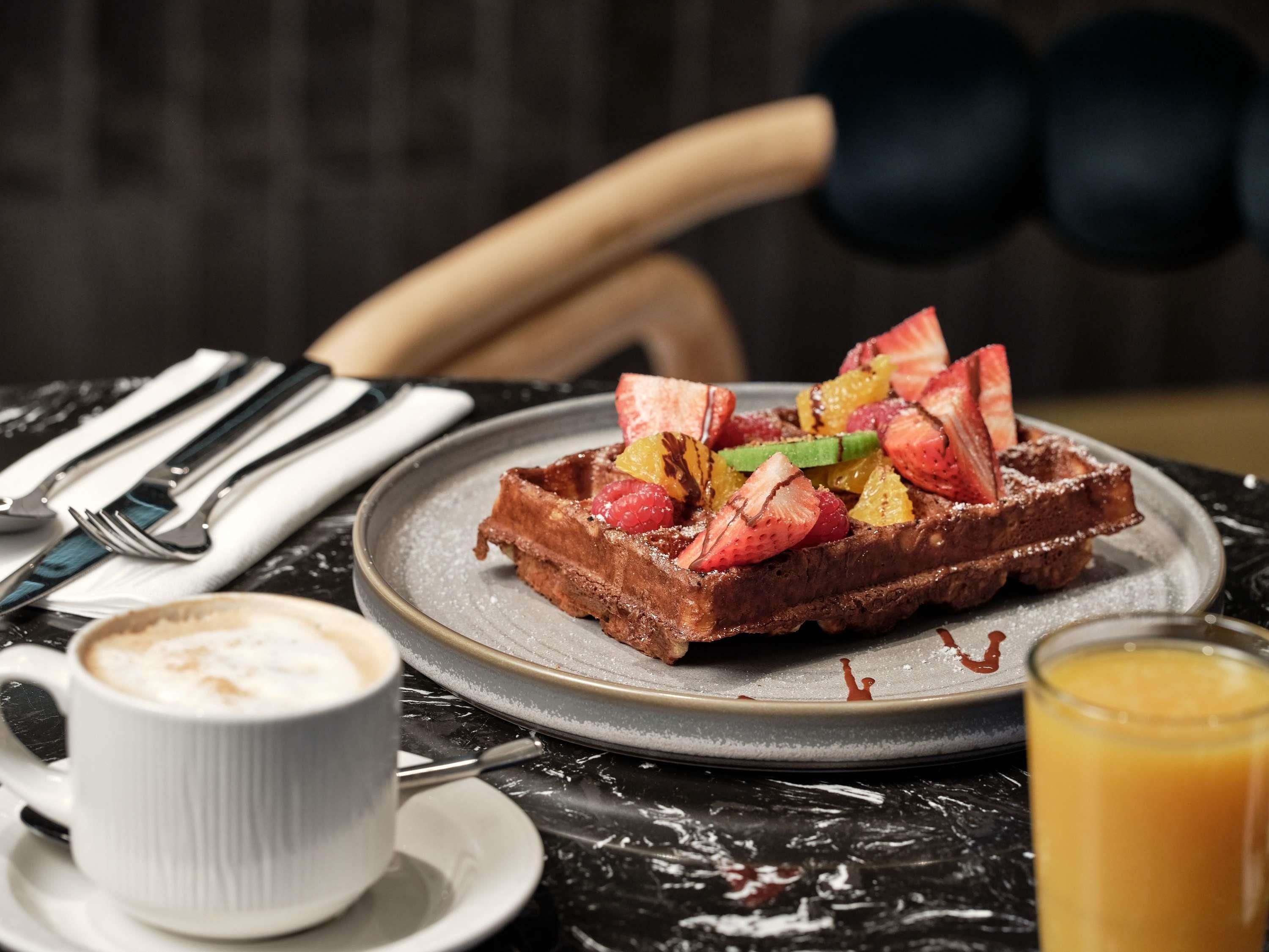 Un waffle con fruta en un plato, una taza de café y un vaso de jugo de naranja sobre una mesa.