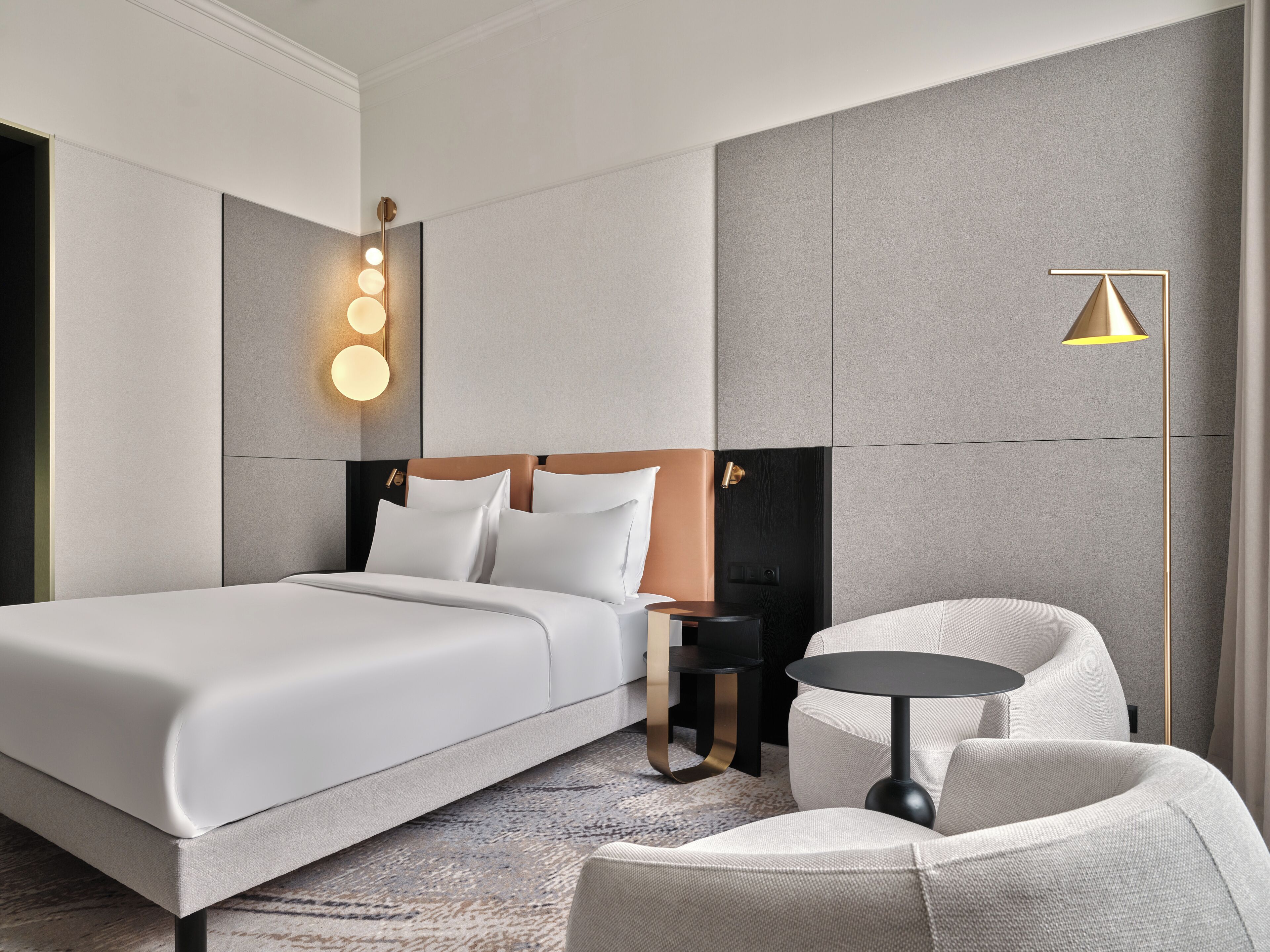 A modern hotel room with a large bed, a bedside table, a chair, and a floor lamp.