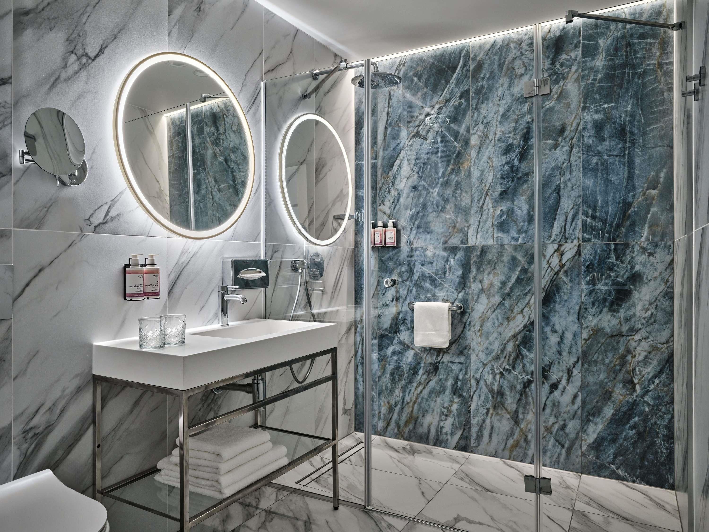 A modern bathroom with marble walls, a glass-enclosed shower, and a vanity with a mirror.