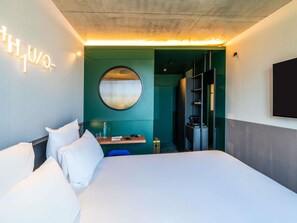 A modern hotel room with a large bed, a round mirror, a desk with a chair, and a wardrobe. - Tribe Paris Clichy  (Clichy)