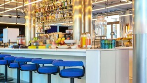 A bar area with multiple stools, a variety of bottles and glasses on shelves, and a water dispenser. - Tribe Paris Clichy  (Clichy)