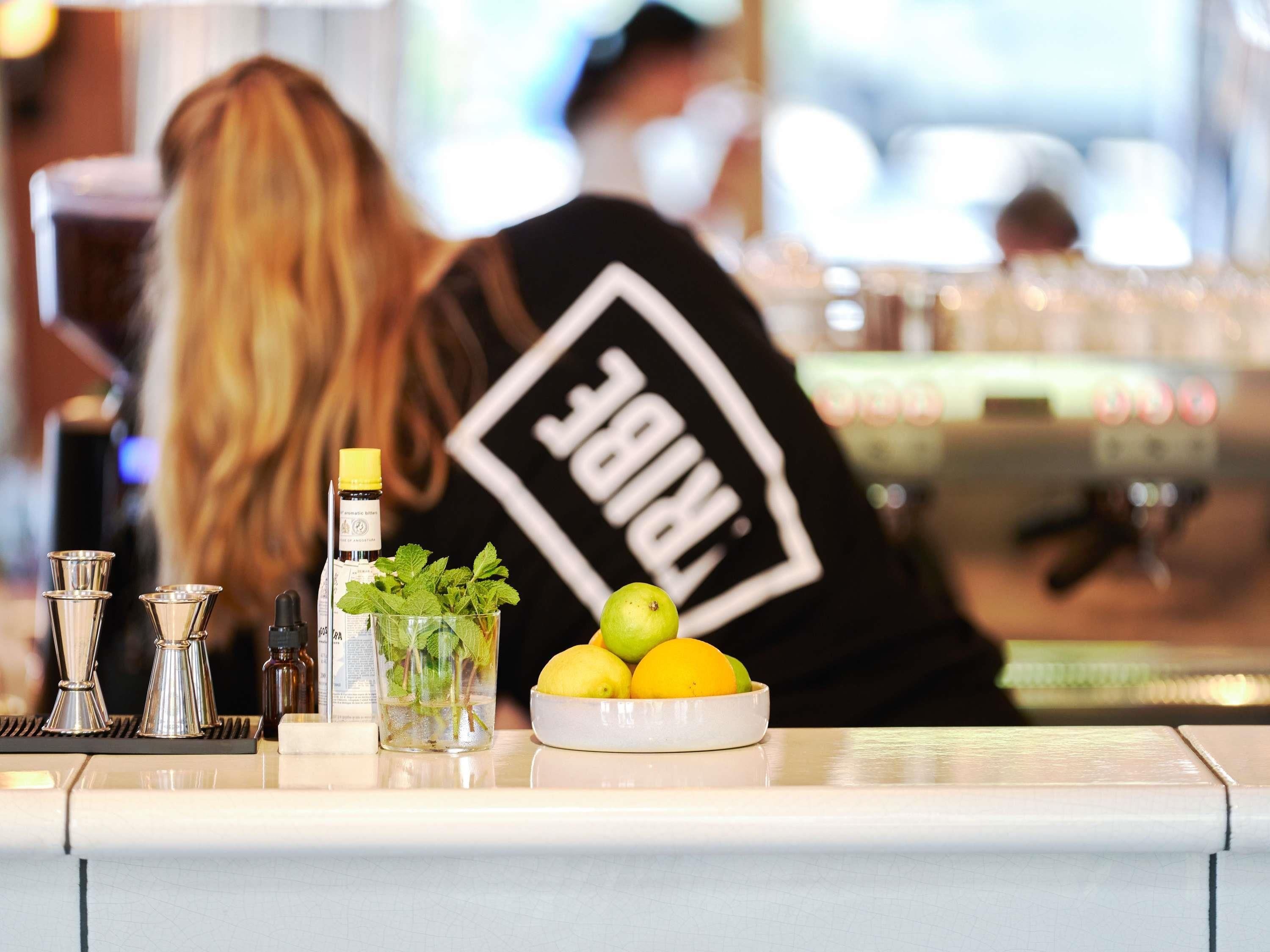 A bar counter with a glass of water, mint leaves, and lemons.