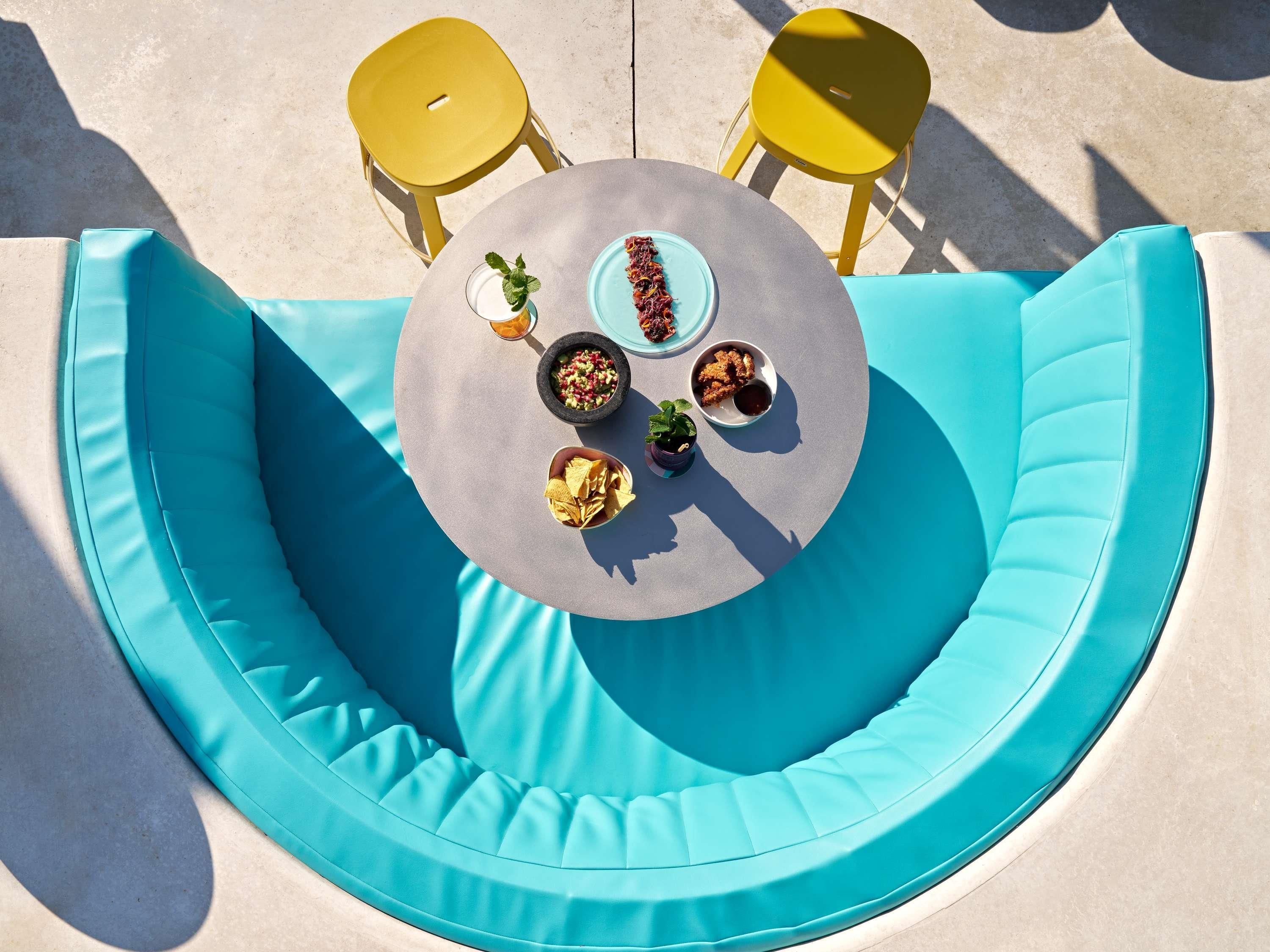A round table with a blue cushioned bench, two yellow chairs, and a variety of snacks and drinks.