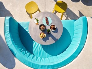 A round table with a blue cushioned bench, two yellow chairs, and a variety of snacks and drinks. - Tribe Paris Clichy  (Clichy)
