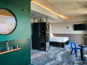 A hotel room with a bed, a TV, a shelf with glasses, and a patterned carpet. - Tribe Paris Clichy  (Clichy)