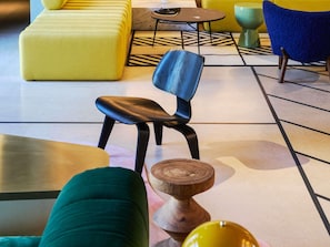 A modern lounge area with a yellow sofa, a blue chair, a round table, and a wooden side table. - Tribe Paris Clichy  (Clichy)