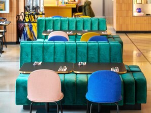 A seating area with green upholstered sofas and chairs, tables with cutlery, and a counter in the background. - Tribe Paris Clichy  (Clichy)