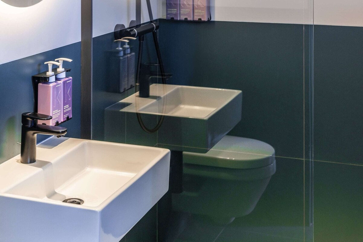 Un baño moderno con ducha envuelta en vidrio, un lavamanos blanco y un inodoro.