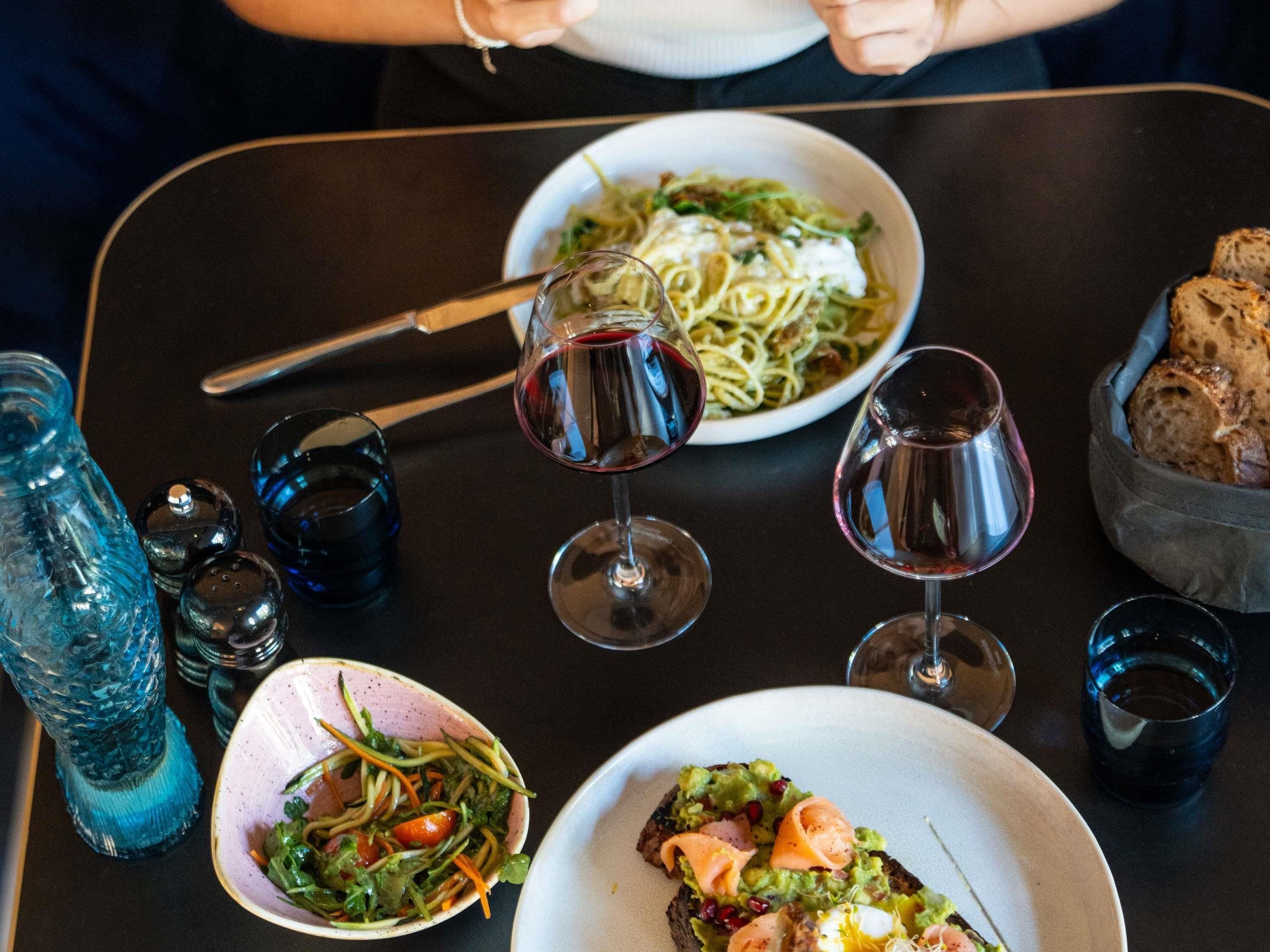 Une table à manger avec différents plats, des verres de vin rouge et une bouteille d’eau bleue.