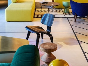 A modern lounge area with a yellow sofa, a blue chair, a round table, and a wooden side table. - Tribe Paris Clichy  (Clichy)