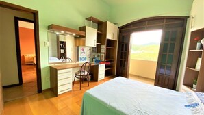 A bedroom with a bed, a desk, and a chair. There is a window with a view of the outdoors.