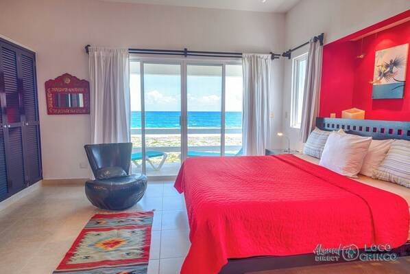 A bedroom with a large bed, a view of the ocean, and a red accent wall. - Vibrant and colorful ocean side villa with pool, AC and much more! (Akumal)