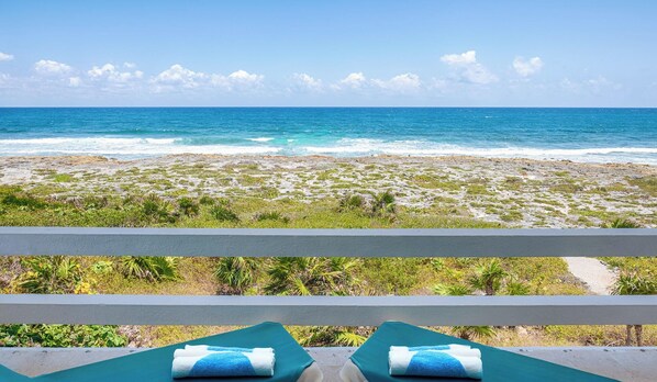 A beach view from a balcony with two lounge chairs and towels, overlooking a sandy beach with sparse vegetation and the ocean. - Vibrant and colorful ocean side villa with pool, AC and much more! (Akumal)