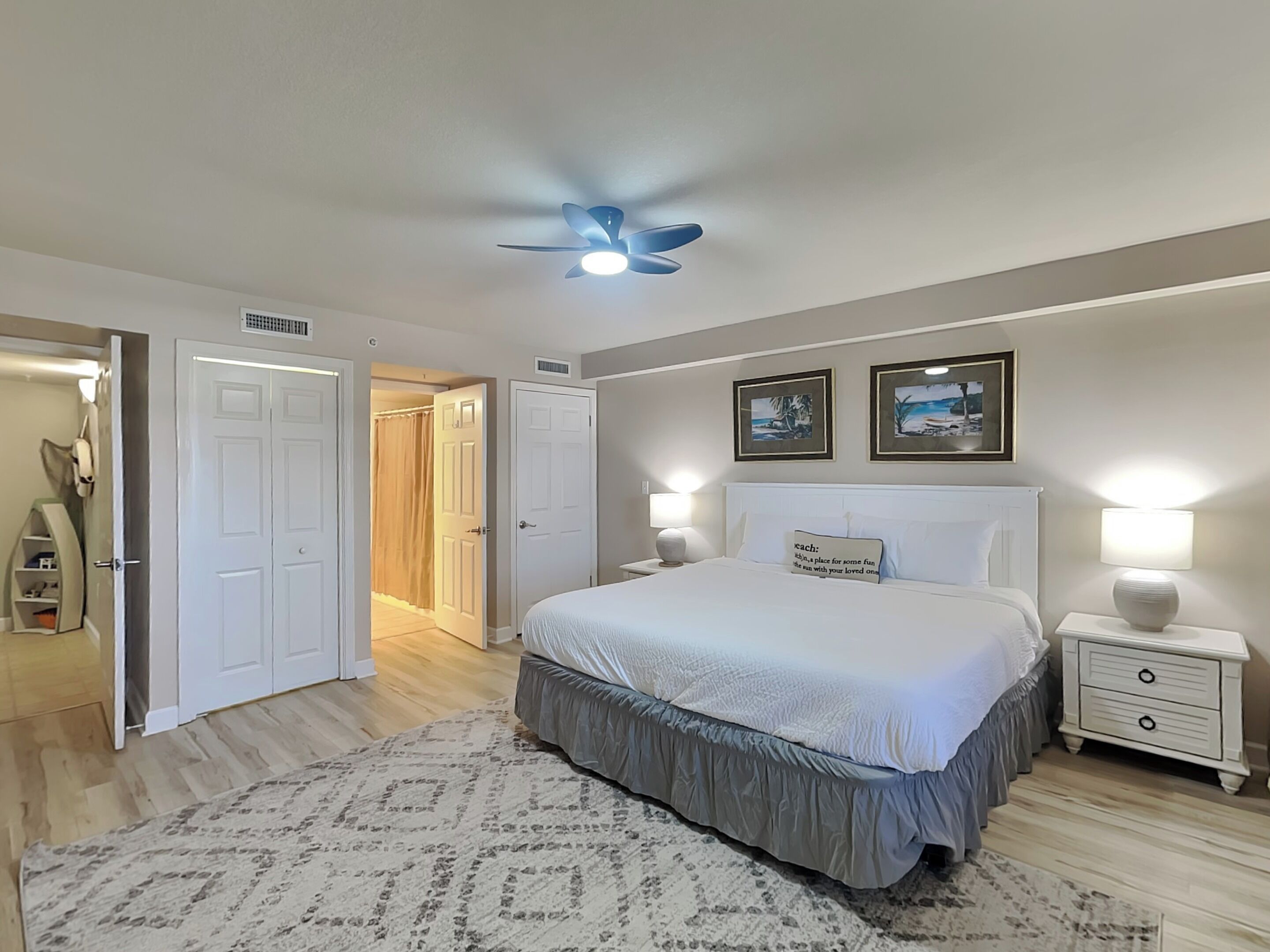 A bedroom with a bed, bedside tables, a ceiling fan, and two framed pictures on the wall.