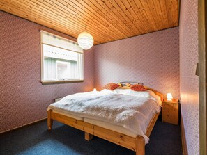 A bedroom with a wooden bed, a window with curtains, a hanging light fixture, and a textured wall. - 6 Person Holiday Home in Fano-by Traum (Fano)