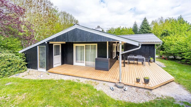 A modern black house with a wooden deck, large windows, and a small outdoor seating area. - 4 Person Holiday Home in Oksbol-by Traum (Oksbol)