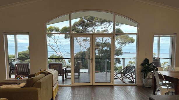 Amplia sala de estar con un gran ventanal corredizo que da a una terraza con mobiliario exterior.