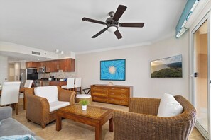 Un salon moderne avec des meubles en osier, un ventilateur de plafond et des œuvres d’art accrochées aux murs.