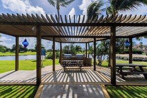 A covered outdoor area with picnic tables and barbecue grills, overlooking a body of water and greenery.