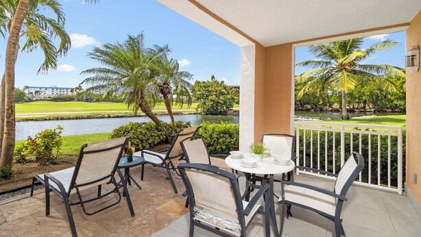 A balcony with outdoor seating, a view of a golf course, and a body of water. - Lake View: 1BR Paradise w/ Patio near Beach, Aruba (Oranjestad)