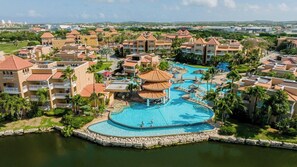 Un complexe hôtelier comprenant plusieurs bâtiments, une piscine centrale et un plan d’eau qui l’entoure.