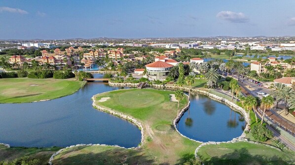 A golf course with water hazards, surrounded by residential buildings and palm trees.