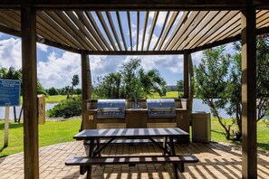 A covered outdoor barbecue area with a grill, a picnic table, and a view of a lake.