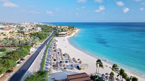 A coastal resort with a beachfront, a road parallel to the beach, and a row of thatched umbrellas. - Lake View: 1BR Paradise w/ Patio near Beach, Aruba (Oranjestad)
