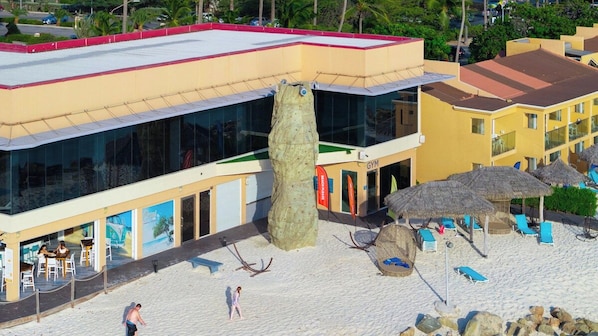 Un hotel con una amplia fachada de vidrio, mobiliario exterior y una zona de playa con tumbonas.