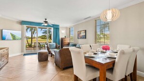 A dining area with a wooden table, white chairs, and a view of a golf course through large windows. - Lake View: 1BR Paradise w/ Patio near Beach, Aruba (Oranjestad)