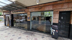 Entrada de hotel con fachada de vidrio, una reja metálica y un contenedor de basura fuera.