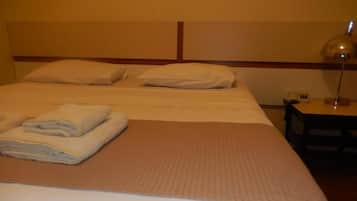 Quarto de hotel com duas camas, uma mesa de cabeceira e um abajur.