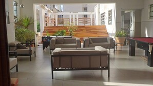 Amplia sala de estar con suelo de madera en patrón de espiga, un sofá seccional beige grande, una mesa de billar y una escalera que lleva a un balcón al aire libre.