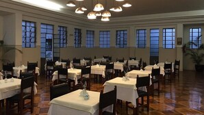Un comedor amplio con varias mesas y sillas, ventanas grandes y lámparas colgantes.