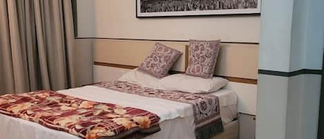 Una cama bien hecha con ropa de cama estampada, un cuadro enmarcado encima y piso de madera.