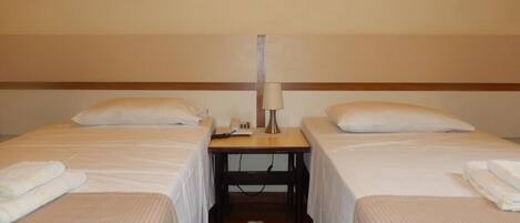 A hotel room with two single beds, a small table with a lamp, and a telephone.