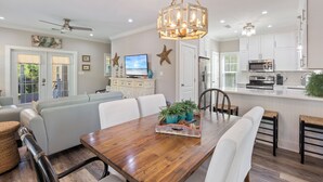 A modern kitchen with white cabinets, a wooden dining table, and a ceiling fan.