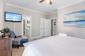 Quarto com uma cama grande, televisão montada na parede e uma pintura de uma cena de praia.