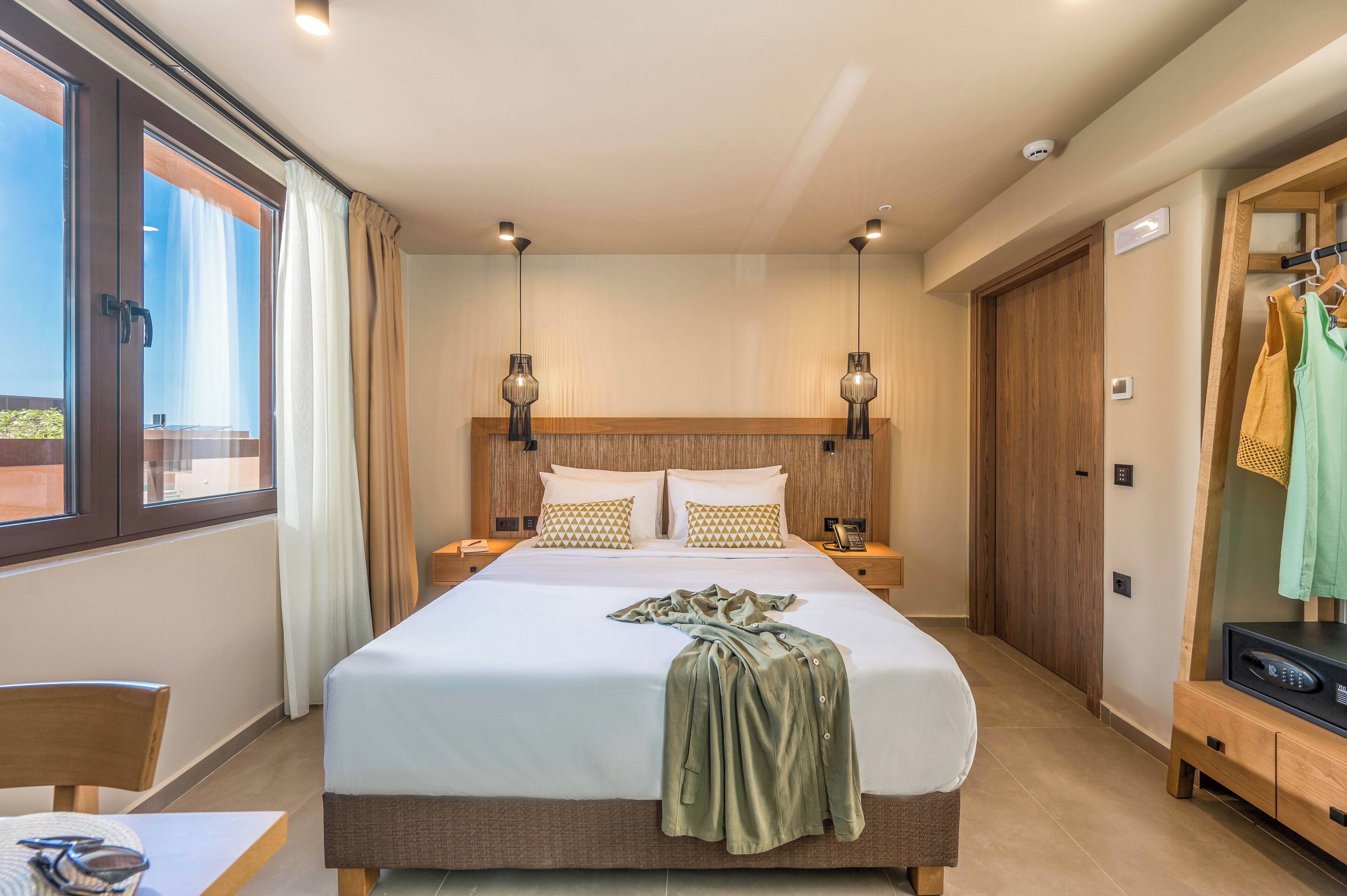 A modern hotel room with a large bed, bedside tables, a wardrobe, and a view of the outdoors.