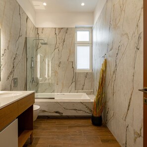 Een moderne badkamer met een marmeren wand, een douchecabine van glas, een houten wastafelmeubel en een kamerplant.