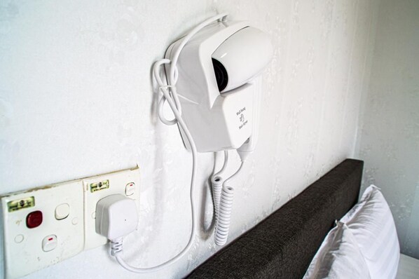 A hair dryer mounted on a wall next to a power outlet with a control panel. - Sammy hoomesaty  (Ipoh)