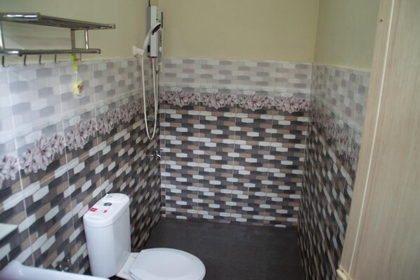 A small bathroom with a toilet, a shower, and a tiled wall with a geometric pattern. - Sammy hoomesaty  (Ipoh)