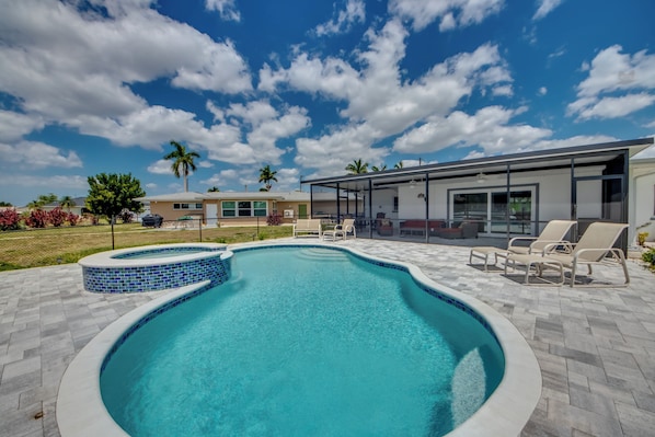 A swimming pool with a tiled edge, surrounded by a patio area with lounge chairs.