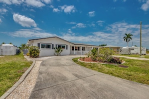 A single-story mobile home with a driveway leading to the entrance, surrounded by a well-maintained lawn and a small garden area.