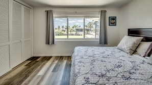 Ein Schlafzimmer mit einem großen Bett, einem Fenster mit Vorhängen, Blick ins Freie und Holzboden.