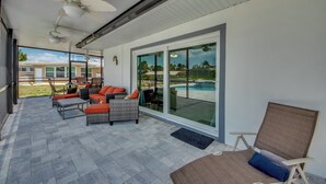 Ein überdachter Patio-Bereich mit Gartenmöbeln, einem Deckenventilator und Blick auf einen Swimmingpool.