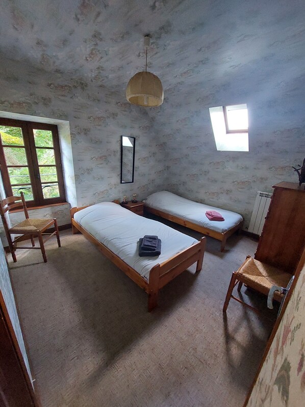 A room with two wooden beds, a chair, a small table, a hanging light fixture, and a window. - la Longere du Haut Courby en Plein Cœur de la Forêt Domaniale de Sédières (Eyrein)