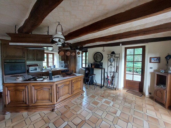 A spacious kitchen with a large island, wooden cabinets, and a tiled floor. - la Longere du Haut Courby en Plein Cœur de la Forêt Domaniale de Sédières (Eyrein)