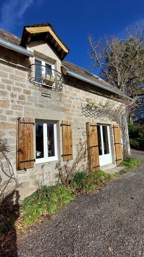 A stone house with wooden shutters, a small balcony, and a gravel driveway. - la Longere du Haut Courby en Plein Cœur de la Forêt Domaniale de Sédières (Eyrein)